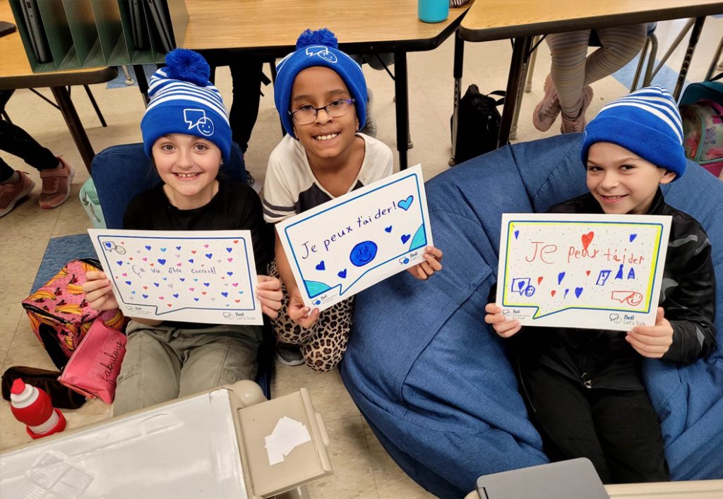 Trois enfants portant des chapeaux bleus tiennent un message qu'ils ont écrit pour la Journée Bell pour la cause.