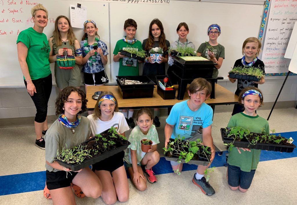 12 enfants et leur enseignant montrent leur travail en faisant pousser différentes plantes, en tenant leurs plantes pour montrer à la caméra.