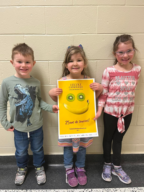 3 jeunes élèves. tiennent l'affiche des écoles catholiques - 25 ans de sourires!