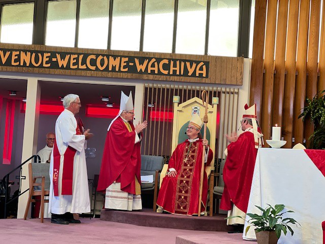 Des prêtres en robes rouges se tiennent devant un panneau de bienvenue pour la Cité du Vatican