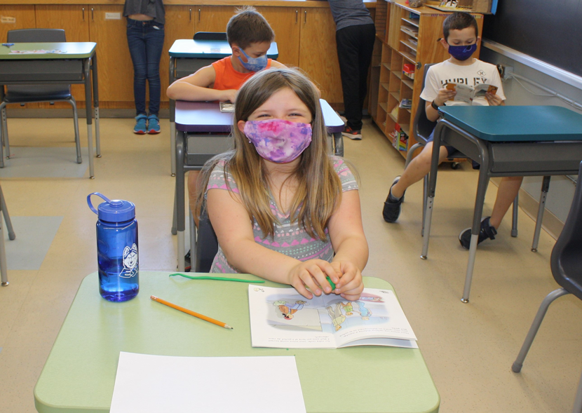 Des élèvent heureux à leur pupitre portant leurs masques