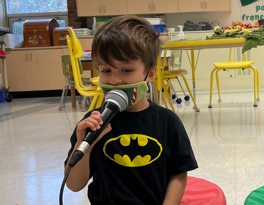 Un petit garçon chante dans le micros avec un masque sur bouche