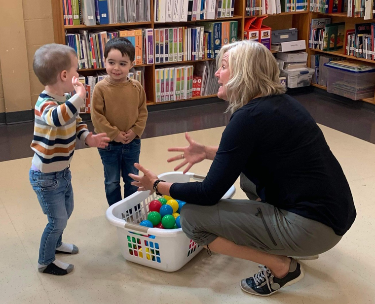 Deux jeunes enfant joue ensemble devant une panier de balle et leur enseignante