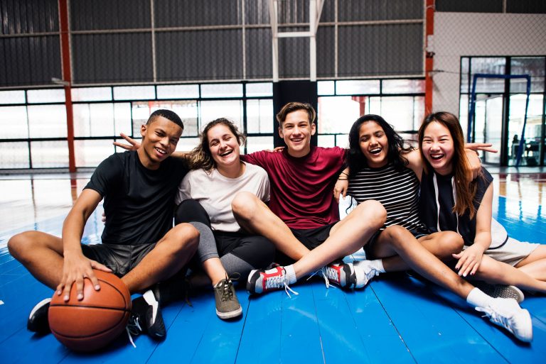 Un groupe d'élève habillé en habit de sport sourit, assit sur un matelas de sport bleu