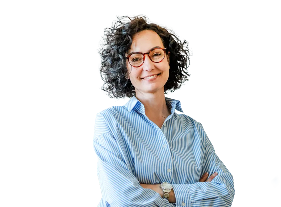 Femme souriante portant des lunettes rouges et une chemise à rayures bleues, les bras croisés, sur fond clair.